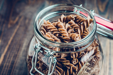 Dark brown pasta in a glass jar in the kitchen