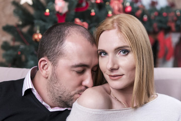 Fototapeta premium Man kisses a woman in a bare shoulder against the background of a Christmas tree