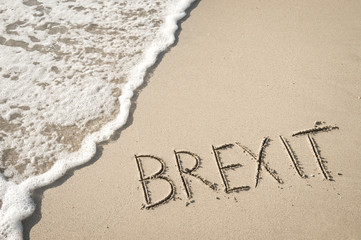 'BREXIT' written in the sand on the beach with the sea washing up the shore.