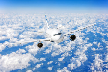 Fototapeta premium Commercial airplane flying over bright blue sky and white clouds.
