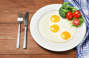 Fried eggs with vegetables on the wooden table