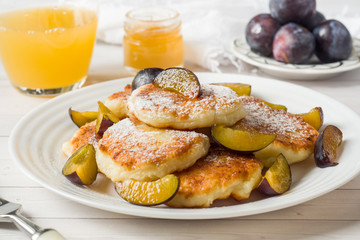 Cheese pancakes in powdered sugar with fresh plums on a plate