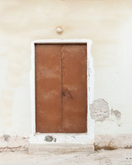 Old brown painted metallic door on weathered wall.