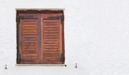 Old wooden window with brown shutters, on rough surfaced wall.