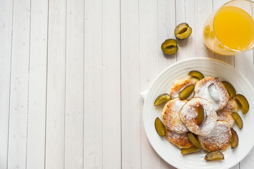 Cheese pancakes in powdered sugar with fresh plums on a plate. Copy space