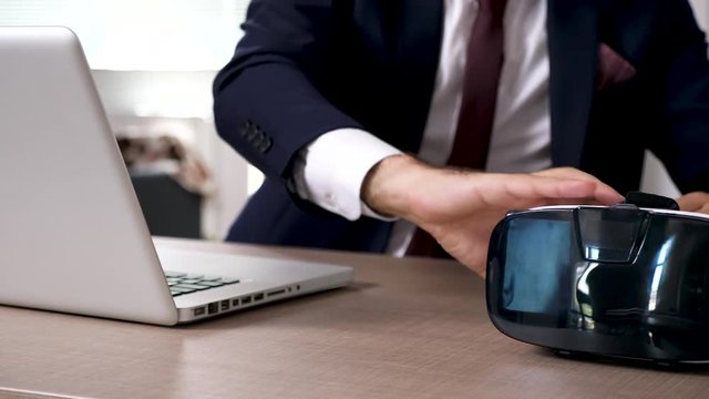 Close up businessman types on computer than picks up a VR headset. Dolly slide footage