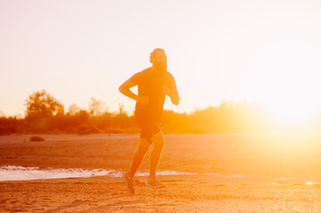 Young bearded man running near sea at sunset