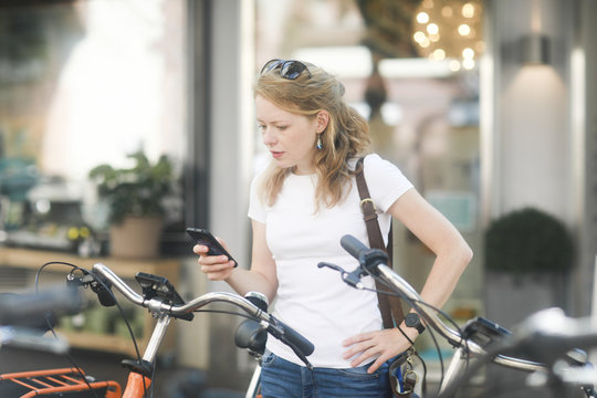 Germany, young woman with smartphone renting a city bike