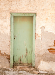 Old green wooden door with cracks, on weathered wall.