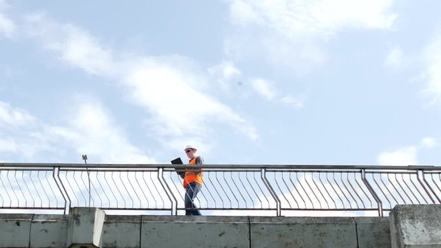 A man inspector walks across the bridge looking around and inspects the quality of the bridge, checks, engineer