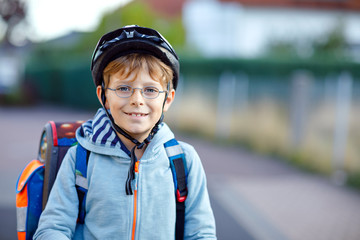 Portrait of beautiful school kid boy with glasses on the way to school building. Happy healthy child wearing safety helmet. Smiling schoolboy of elementary class