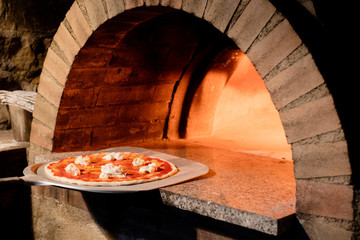 Freshly made pizza being put into hot pizza oven