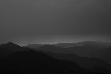 layers of mountain ranges with heavy clouds above black and white