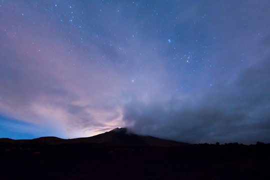 Vulkan unter Sternen und Wolken bei Nacht