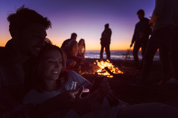 Fototapeta premium Couple enjoying bonfire with friends on beach
