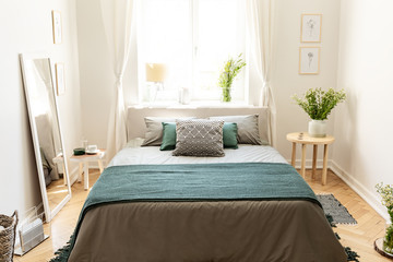 A big bed dressed in earth colors linen with cushions and a blanket standing in an eco friendly...