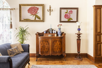Real photo of an antique cabinet with porcelain decorations, paintings with roses and blue sofa in...