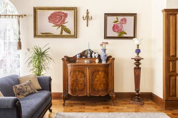 Fotobehang Real photo of an antique cabinet with porcelain decorations, paintings with roses and blue sofa in a living room interior © Photographee.eu