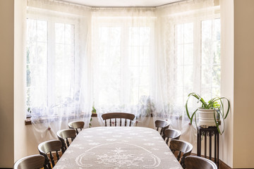 Old style dining room interior with a big window decorated with curtains, table with chairs and plant. Real photo