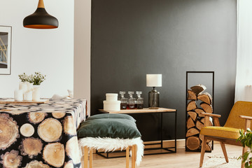 Table and stool in black and white dining room interior with yellow armchair and lamps. Real photo