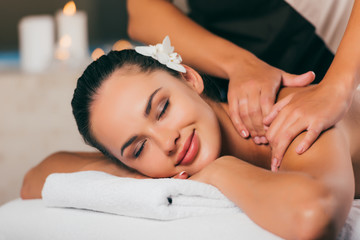 Obraz na płótnie Canvas beautiful woman with flower in hair having massage at spa salon