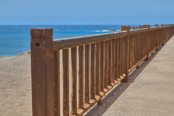 Obraz premium Views from the viewpoint of Punta de Jandia with wooden railing located on a cliff and background rock formations in the blue sea in Fuerteventura, Canary Islands, Spain