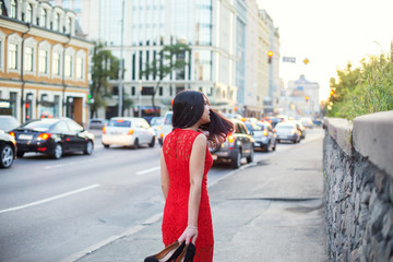Obraz premium A slender girl in a red dress is walking along the sidewalk.