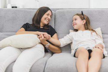 Mother and daughter are having a lot of fun in the living room sitting on the grey couch. mother and daughter holding hands