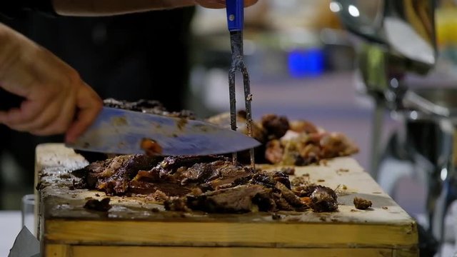Close up on hands holding a smoked brisket on a cutting board, quickly slicing cooked meat into thin slices for a barbecue plate in a restaurant.