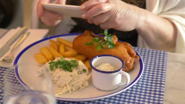 Woman taking photos of fish and chips dinner by smartphone in 4k slow motion 60fps