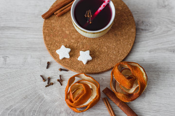 Red mulled wine on a cork stand on a wooden background with various spices, cinnamon sticks, sugar, orange peel, clove seeds.