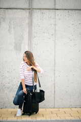 Woman sitting on luggage at street and waiting for bus.