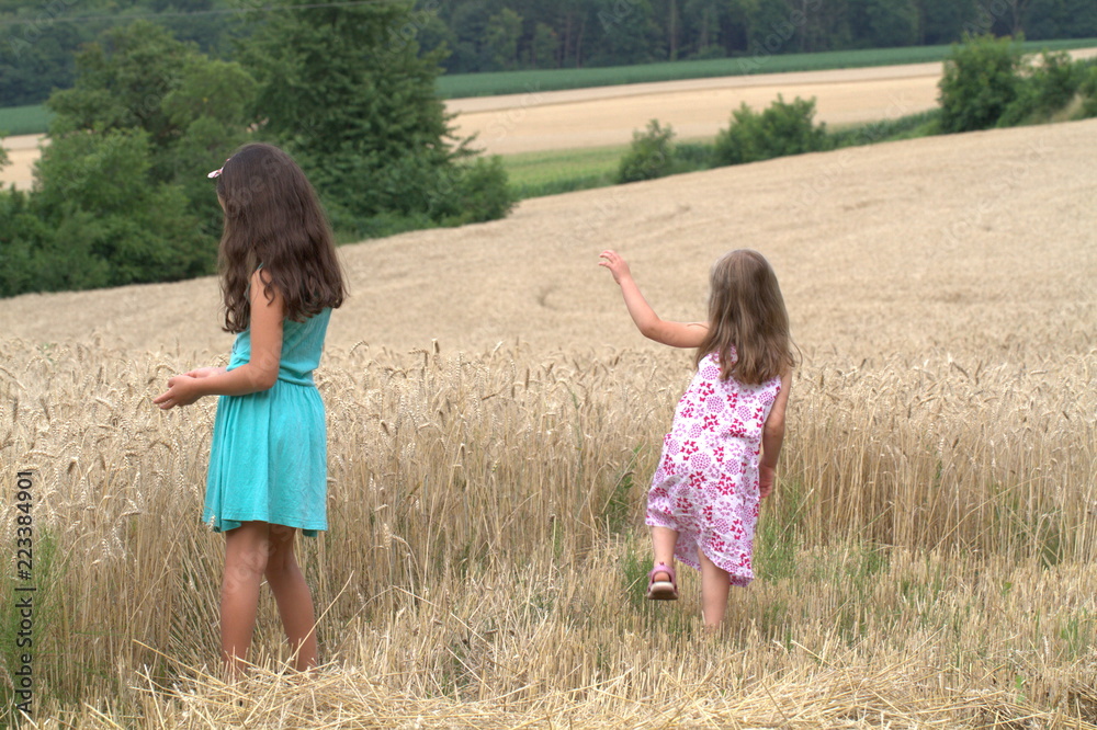 Wall mural two little girls sister walking on a wheat field