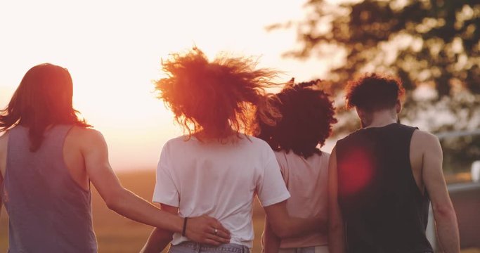 Group of friends , have a great time together in the middle of field with amazing sunset walking through the grass happy and smiling , beside are a orange van. 4k
