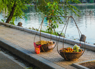 Two loaded shoulder baskets full of fruits stand on the sidewalk near the lake 