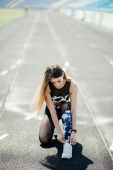 Fototapeta premium Female athlete tying her shoe laces on running track on a sunny day on stadium