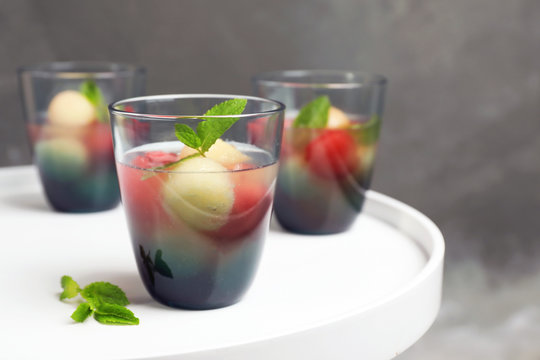 Glasses with tasty melon and watermelon ball drink on light table against color wall