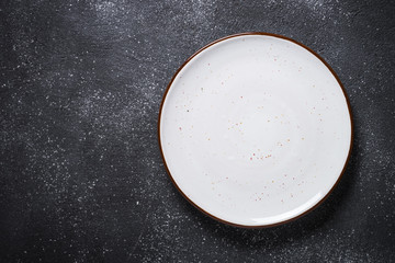 Empty white plate on dark stone table top view.