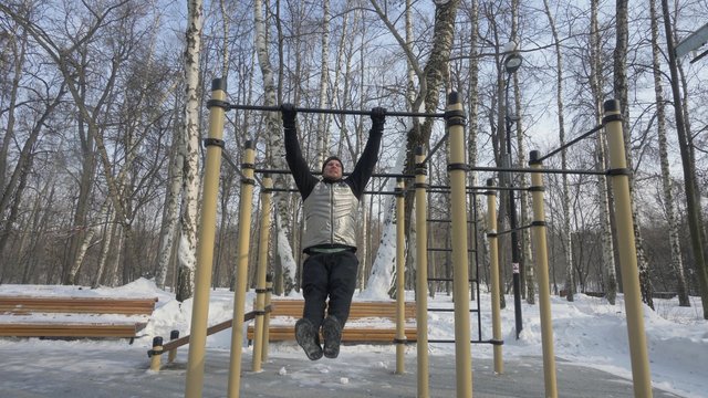 Bearded man doing pull up exercise during outdoor training on sport ground
