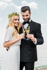 smiling wedding couple clinking with glasses of champagne on beach
