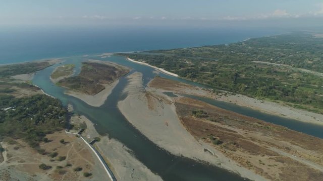 Aerial view of rver flowing into the sea in Philippines,Luzon. ropical landscape with sandy coast and river among farmer fields flowing into the blue ocean