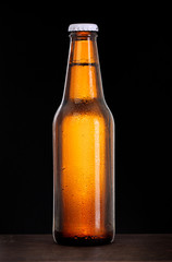 Cold beer bottle with condensation of water drops on black