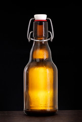 Cold swing top beer bottle with condensation of water drops on black