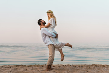 Fototapeta na wymiar side view of groom holding bride and they looking at each other on beach