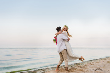 Fototapeta na wymiar groom hugging and spinning around happy bride on beach