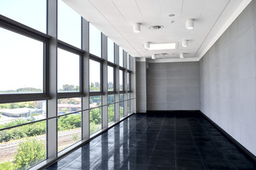 Big empty office space with window wall. Day light illumination. Grey tones interior design. Dark and light color scheme. Window reflection on glossy floor. Perspective front view. Modern business