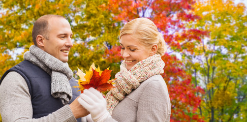 love, relationships and people concept - smiling couple with maple leaves over autumn park background