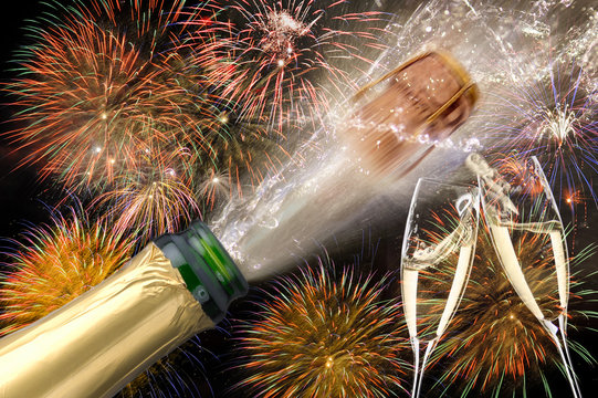 Champagnerflasche mit poppendem Korken und Sektgläser beim Anstossen vor Brillantfeuerwerk zu Neujahr 2019
