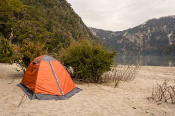 Camping orange tent in a campsite near a lagoon / Camping gear / Camping on the beach next to a lake with cloudy sky