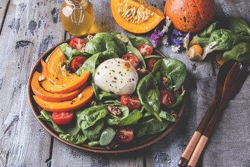 salad with baked pumpkin, mozzarella cheese, spinach greens, tomatoes in a plate on a wooden table